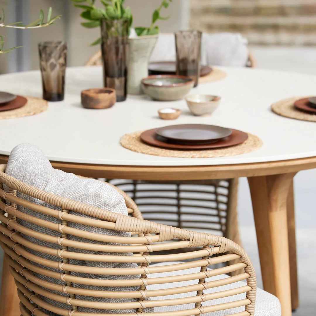 "Neutral-toned dining setup featuring woven rattan chairs, wooden accents, and textured tableware against a light backdrop."