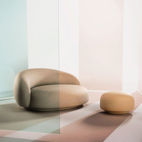 Soft beige curved sofa and round ottoman on a pastel geometric background with cool blue and warm pink tones.