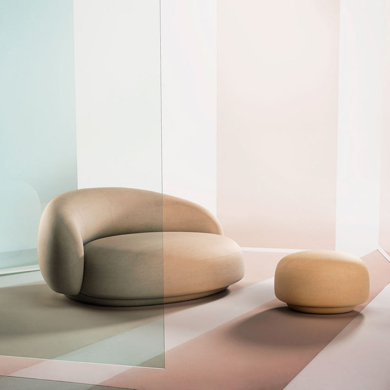Soft beige curved sofa and round ottoman on a pastel geometric background with cool blue and warm pink tones.