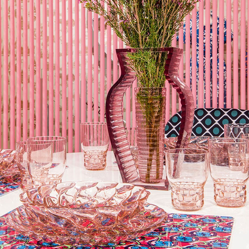 Rose-hued glassware set with intricate patterns, displayed on a vibrant, colorful tablecloth against a pink backdrop.