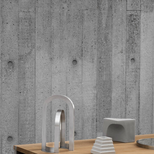Gray concrete wall with textured pattern, featuring minimalist silver and gray decor on a wooden table.