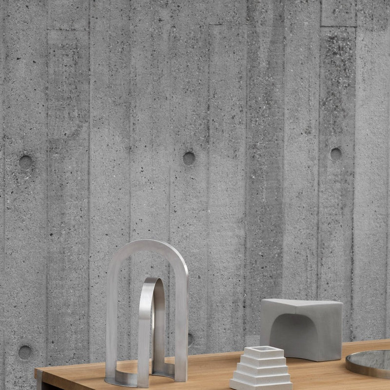 Gray concrete wall with textured pattern, featuring minimalist silver and gray decor on a wooden table.