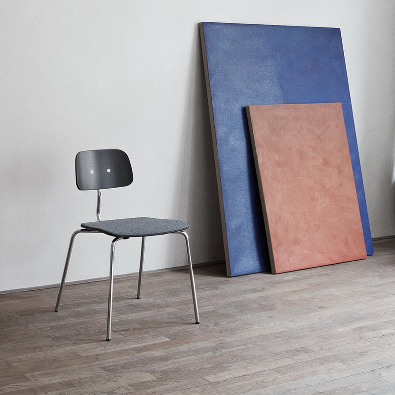 Gray chair with a minimalist design, set against blue and terracotta panels on a wood floor. Simple and modern color palette.
