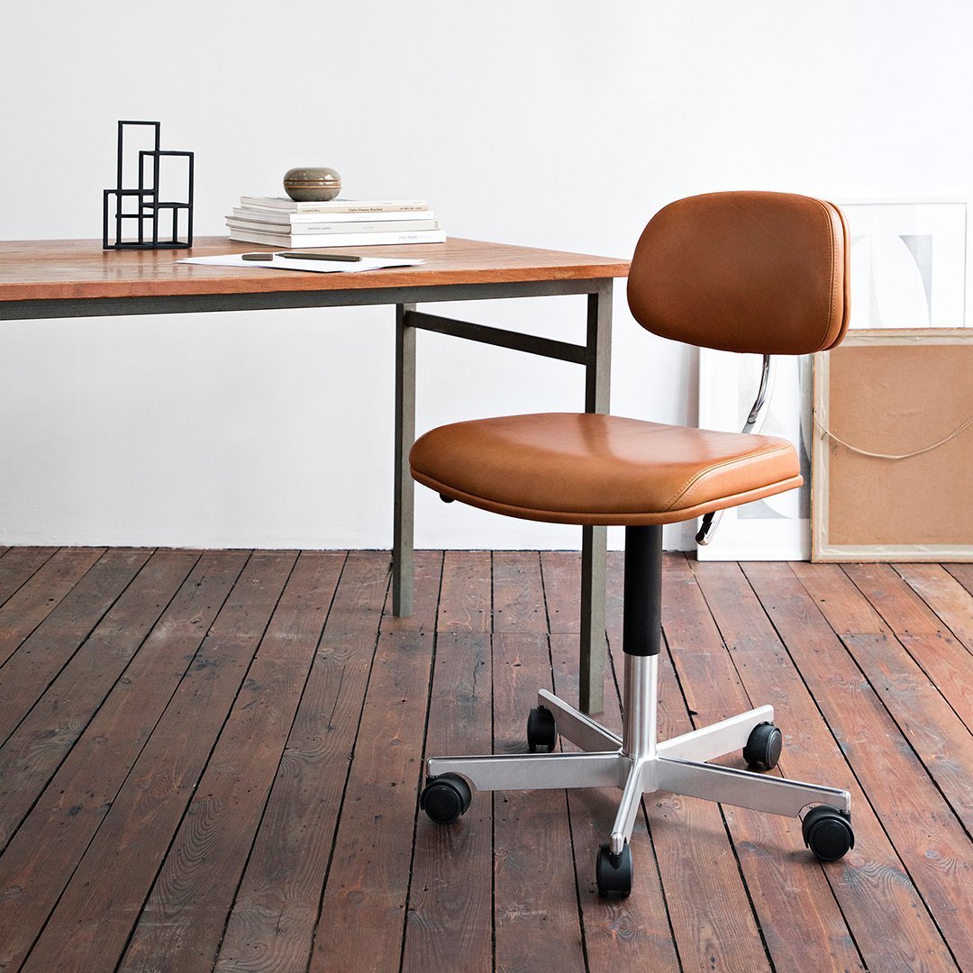 Brown leather rolling office chair on a wooden floor, featuring a sleek silver base and minimalist design.