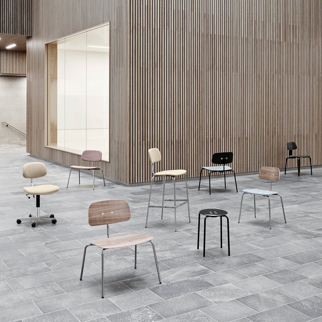 Colorful chairs in various hues, including pastel pink, blue, black, and natural wood, arranged in a modern setting.