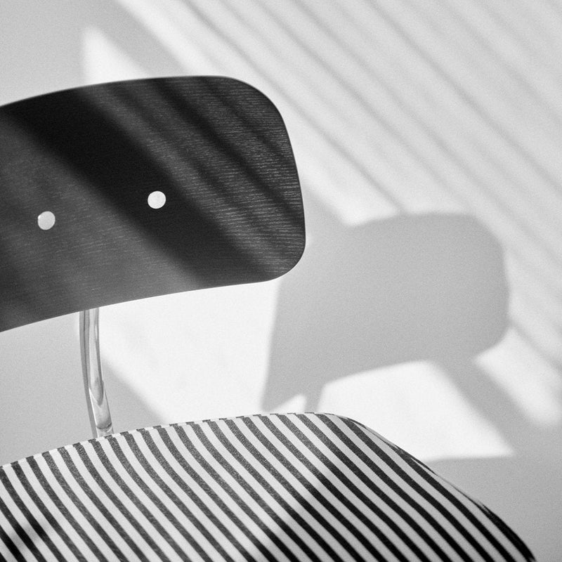 Black chair with a minimalist design, featuring a smooth surface and a striped black and white patterned seat.
