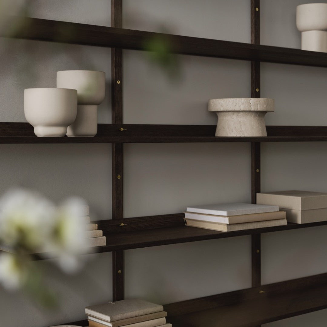 Dark wood shelf with cream and beige decorative bowls and stacked white books on a neutral background.