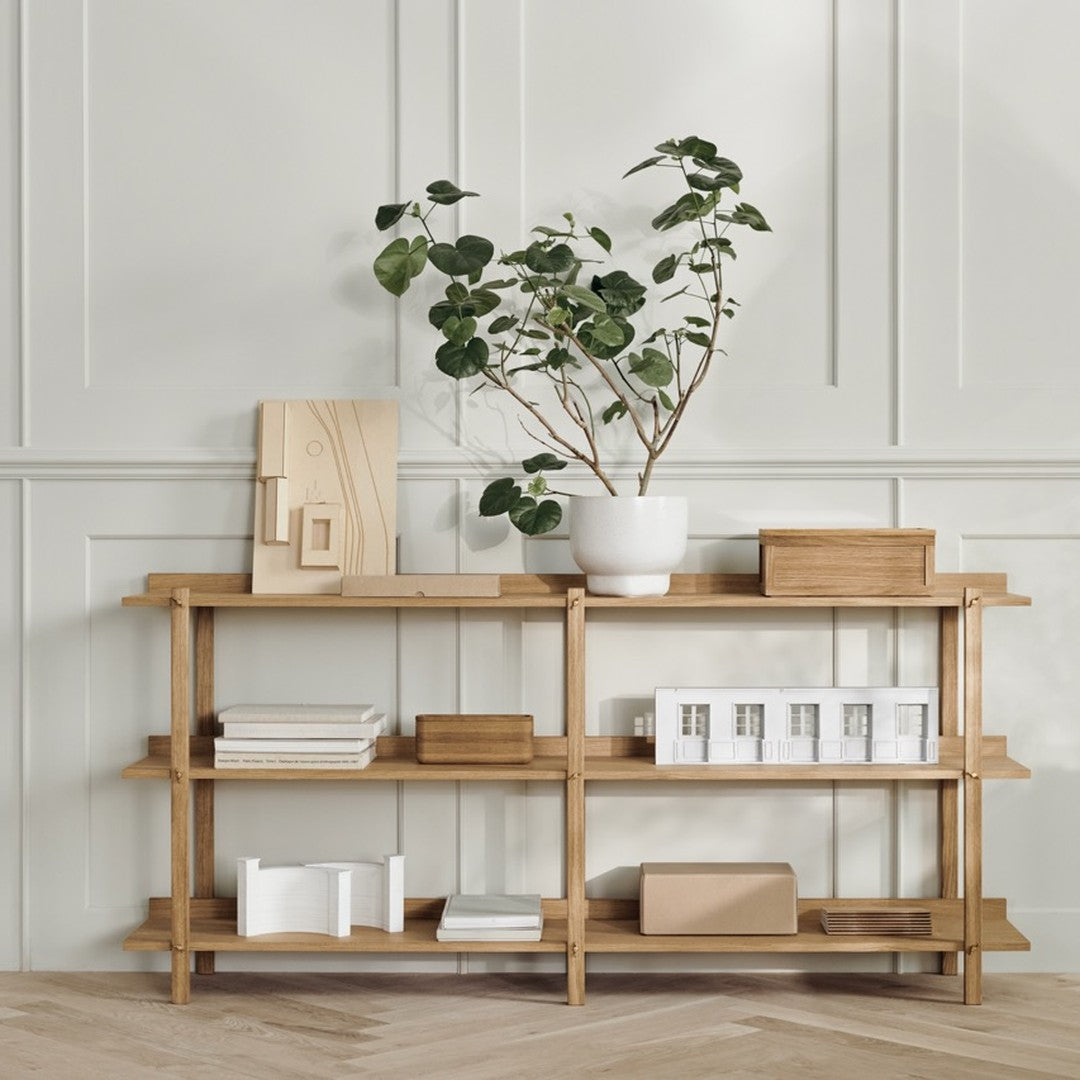 Natural wood shelving in light tones with white and beige decorative accents, accented by greenery. Modern minimalist design.