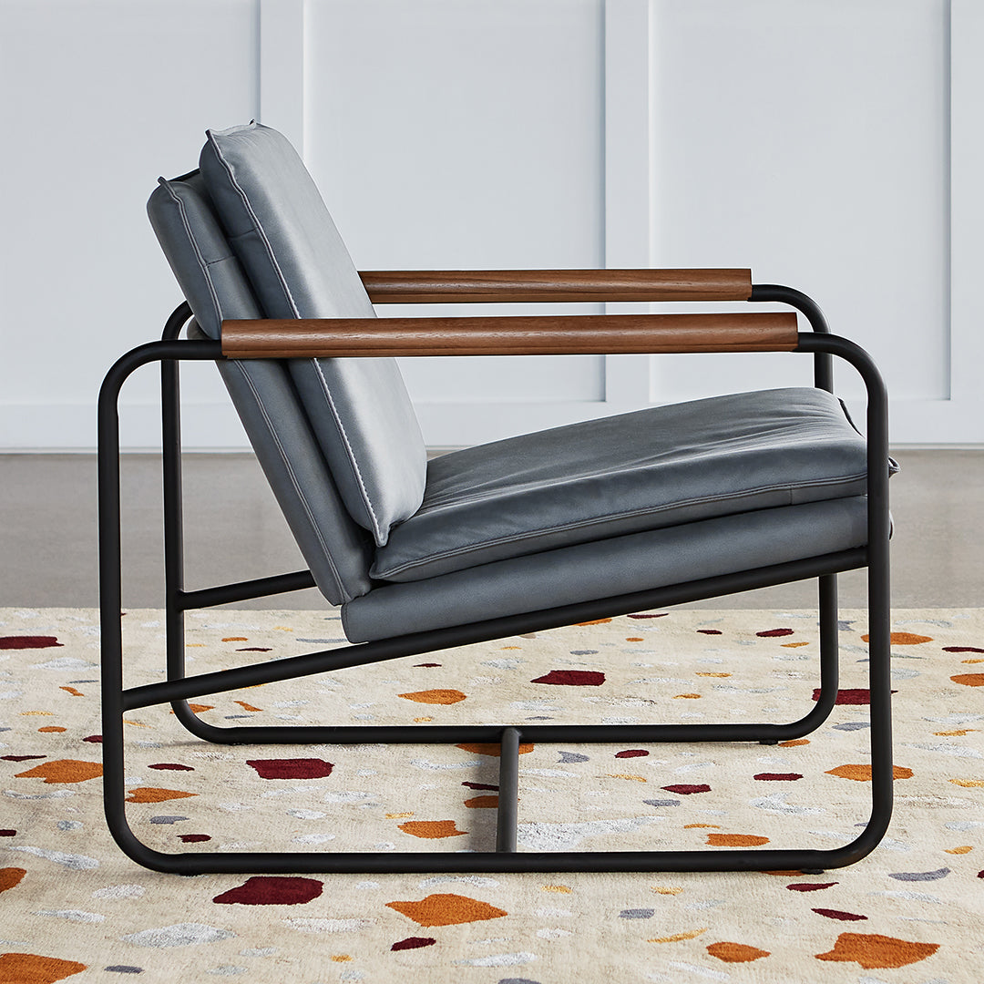 Gray upholstered chair with wood armrests, set on a multicolored, abstract patterned rug featuring warm tones.
