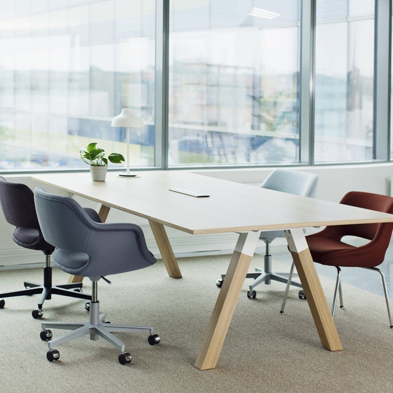 Modern office furniture featuring a light wood table, grey and burgundy chairs, and a minimalist design in a bright setting.