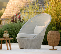 Light gray woven chair with a curved design, complemented by a neutral cushion and a natural wicker side table.