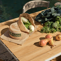 "Natural wood table with fresh greens and pears, featuring earthy tones and subtle textures in a sunlit outdoor setting."