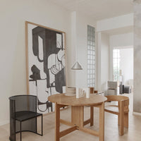 Modern dining area featuring a wooden round table, black mesh chair, and abstract monochrome wall art. Soft neutral tones.
