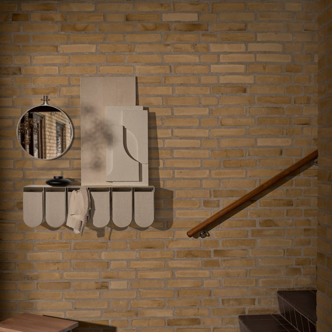 Light beige wall shelf with rounded edges, complemented by a round mirror and subtle textures against a brick backdrop.