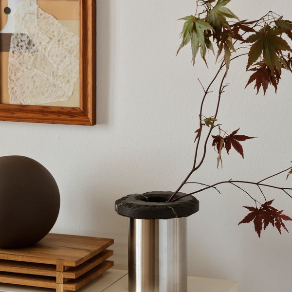 Modern stainless steel vase with a textured black rim, displaying vibrant red maple leaves against a neutral backdrop.