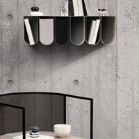 Modern wall shelf in black and gray, featuring curved compartments against a textured concrete wall, minimalist design.