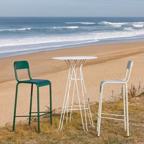 Green and white bar stools with a sleek white table, set against a beach backdrop with waves and sandy tones.