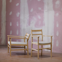 Light wooden chairs against a soft pink wall with abstract white patterns. Elegant and modern design.