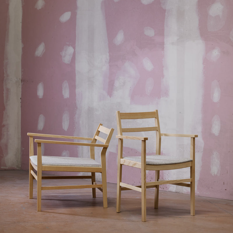 Light wooden chairs against a soft pink wall with abstract white patterns. Elegant and modern design.