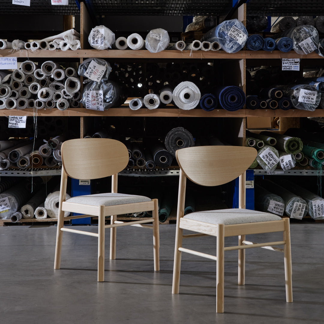 Natural wood chairs with white cushions, set against a backdrop of colorful fabric rolls and patterns.