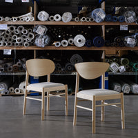 Natural wood chairs with white cushions, set against a backdrop of colorful fabric rolls and patterns.