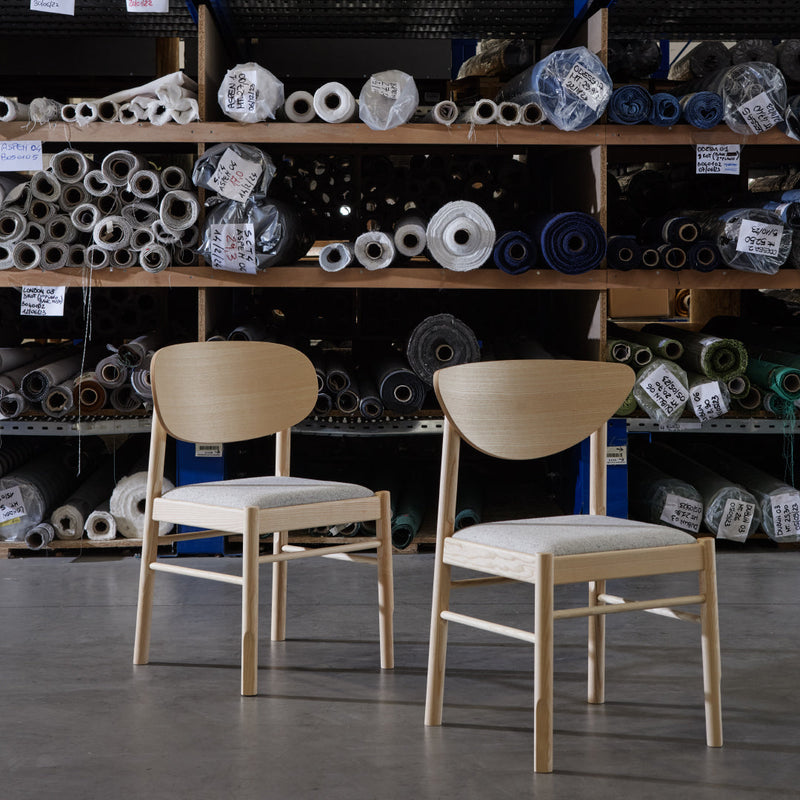 Natural wood chairs with white cushions, set against a backdrop of colorful fabric rolls and patterns.