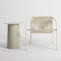 Cream-colored chair with vertical slats beside a pale green cylindrical side table. Modern, minimalist design.
