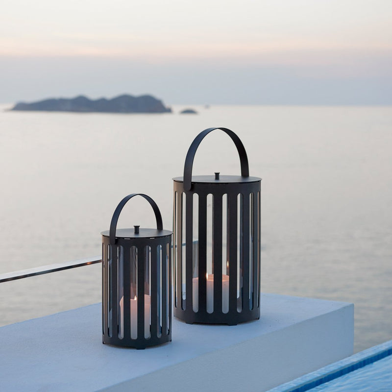 Black metal lanterns with vertical slats, set against a serene ocean backdrop at dusk.