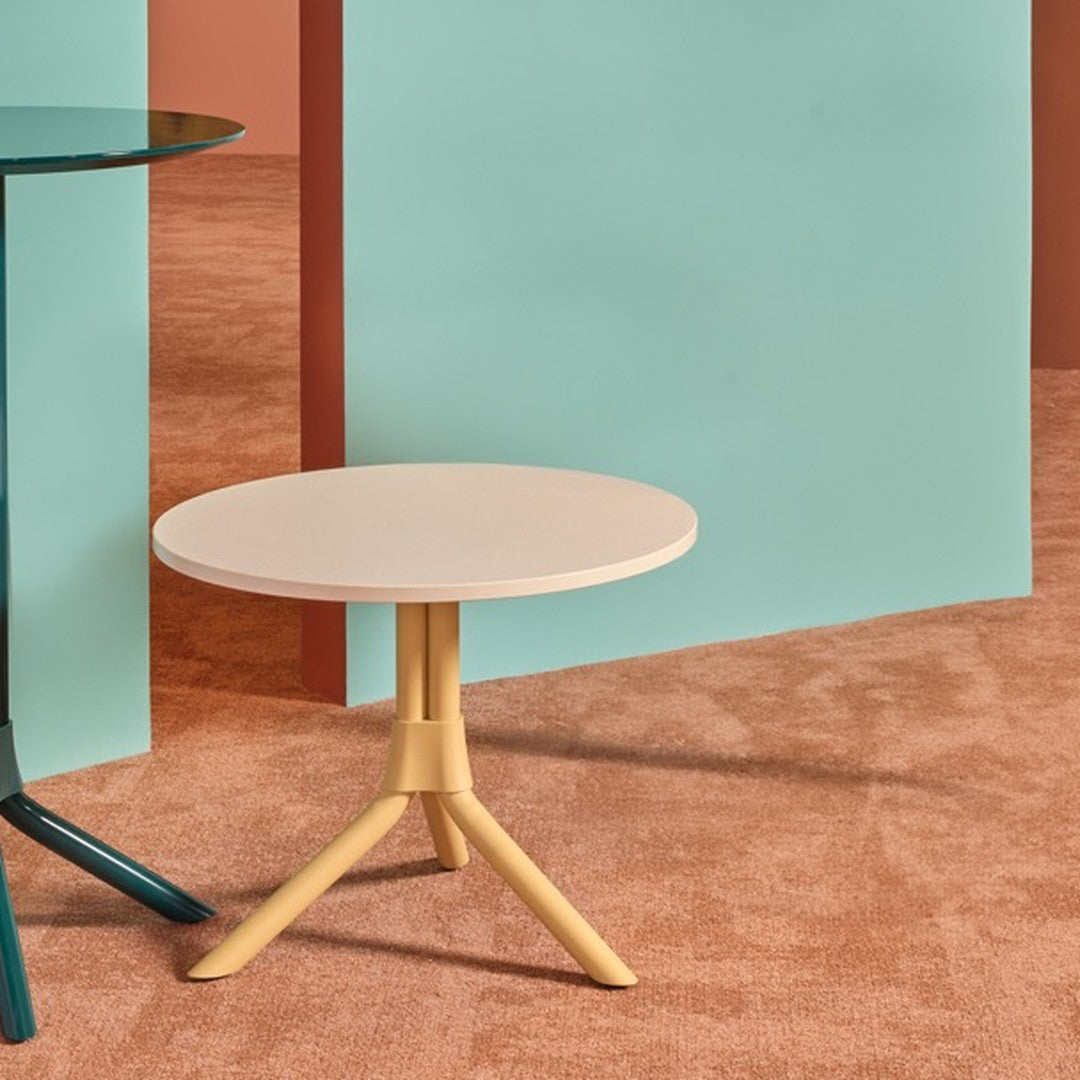 Two modern round tables: one in teal with a glass top, the other in cream and yellow, set against pastel backdrops.