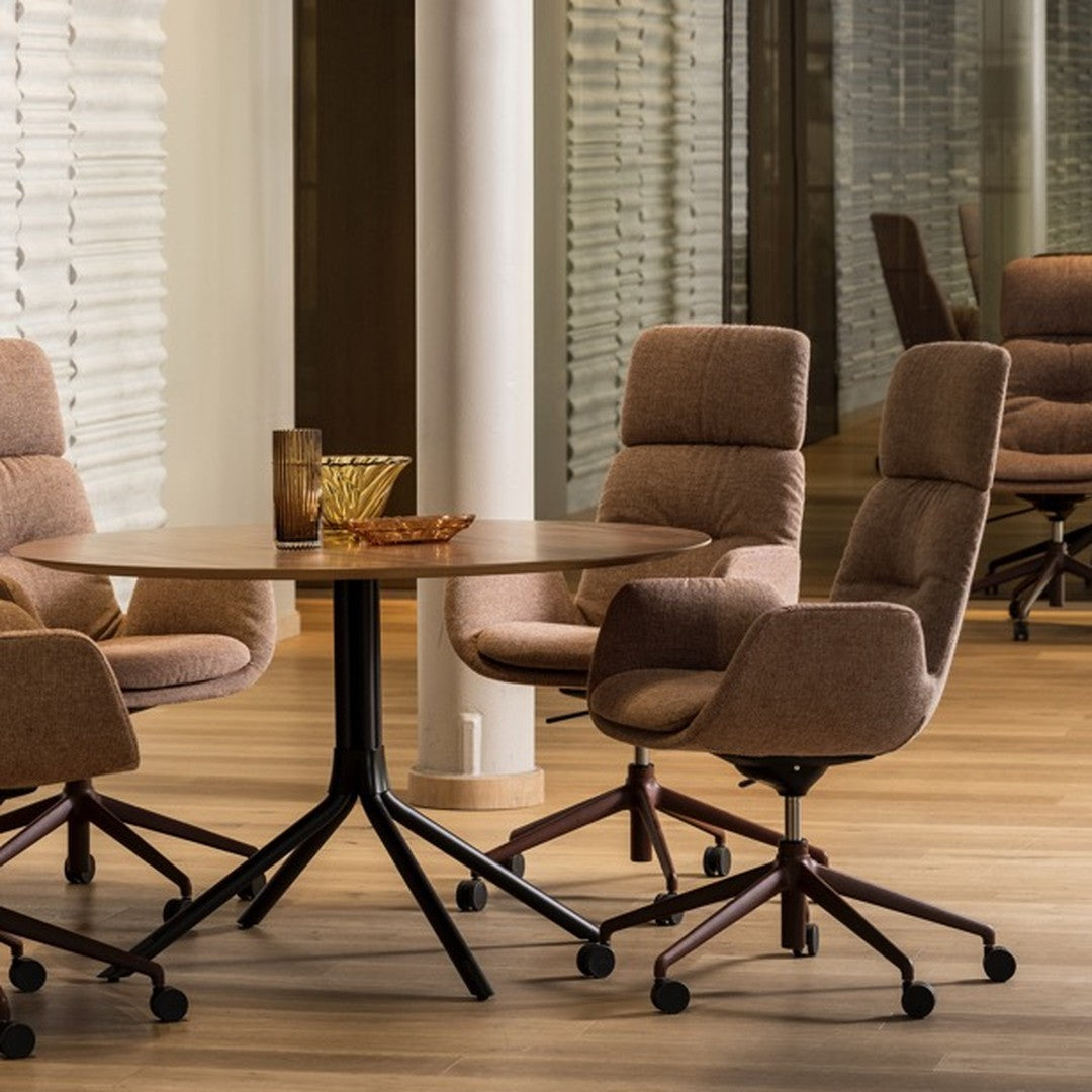 Brown upholstered chairs around a wooden round table, featuring a black base and warm, neutral tones in a modern setting.