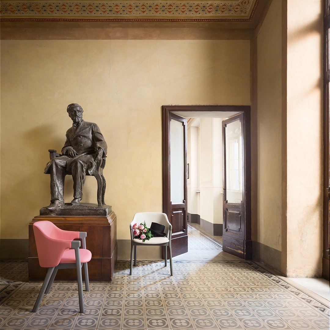 Elegant pink chair beside a vibrant floral arrangement in a refined room with intricate tiled floor and soft earth-toned walls.