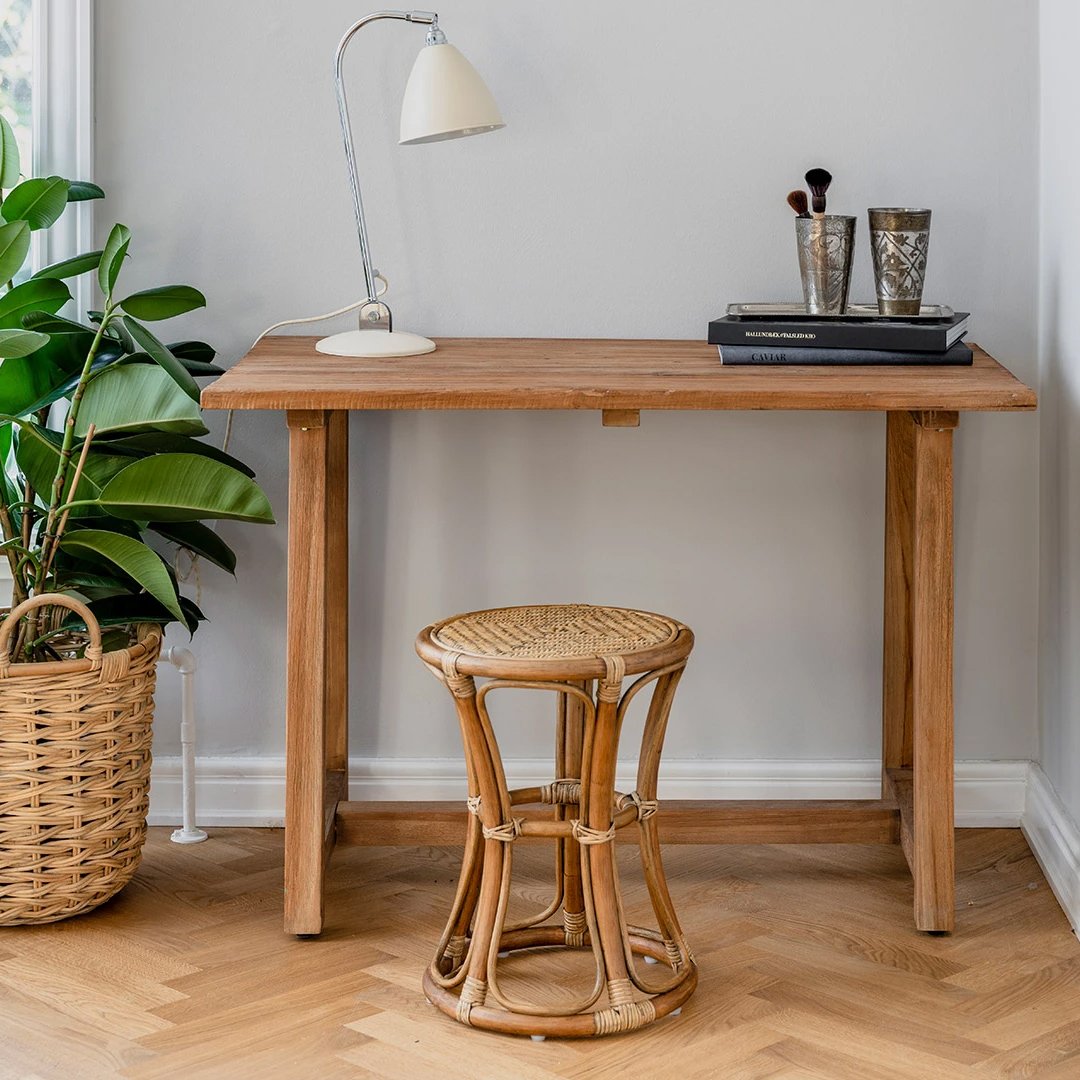 "Wooden desk and rattan stool in natural tones, with a green plant and soft gray wall backdrop."
