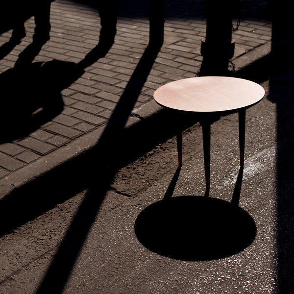 Minimalist round table in soft pink shade casting a distinct shadow on a textured pavement.