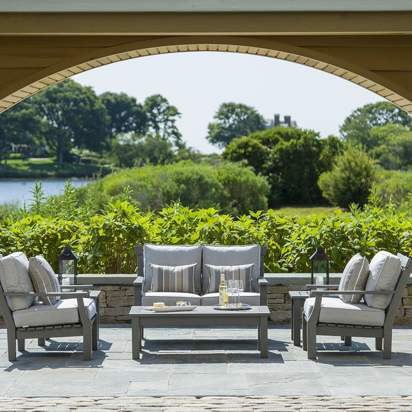 Gray outdoor furniture set with striped cushions, surrounded by lush greenery and serene water views.