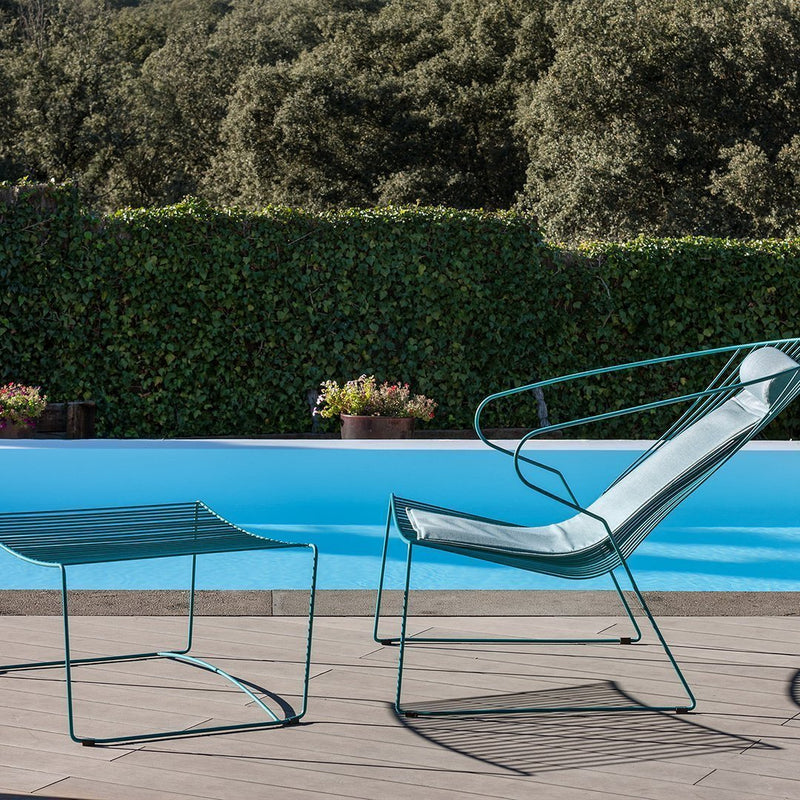 Modern steel lounge chair and side table in teal against a blue pool, featuring sleek lines and minimalistic design.
