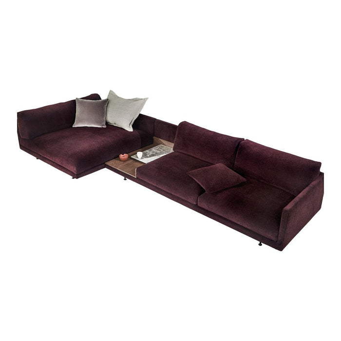 Plush burgundy sectional sofa with soft texture and accent pillows in muted tones, featuring a sleek wooden side table.