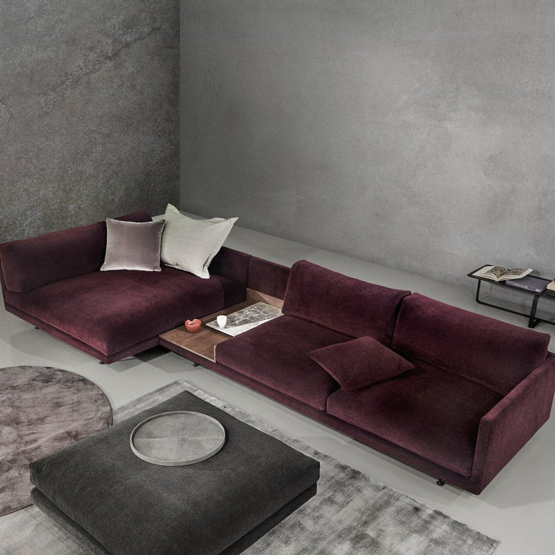 Plush burgundy sectional sofa with textured pillows on a minimalist gray backdrop, featuring circular and rectangular patterns.
