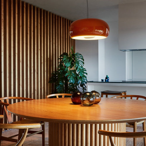 Warm orange pendant lamp, natural wood tones, and green plant in a modern dining area with vertical wood slats.