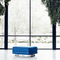 Vibrant blue ottoman with sleek lines, set against a minimalist white backdrop and large windows.