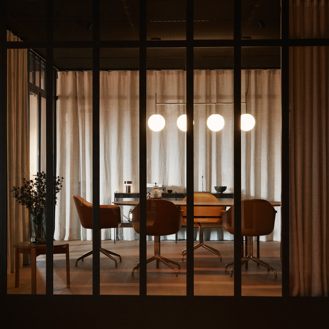 Modern office space featuring warm brown chairs, soft beige curtains, and sleek black accents. Unique light fixtures enhance ambiance.
