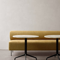 Yellow upholstered sofa with clean lines and two round marble-top tables on black metal bases. Minimalist design.