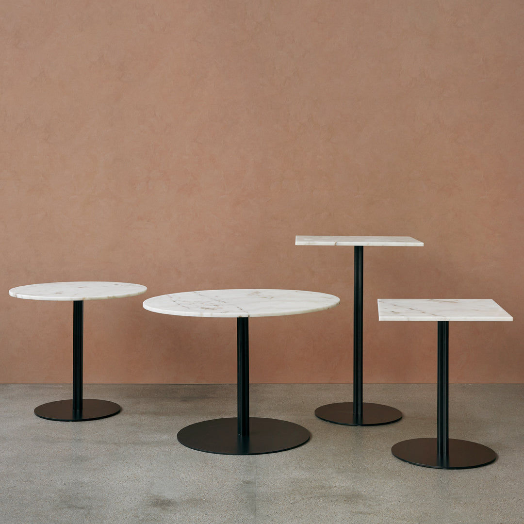 Set of three modern tables featuring white marble tops and sleek black bases against a warm, earthy backdrop.