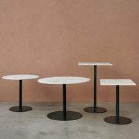 Set of three modern tables featuring white marble tops and sleek black bases against a warm, earthy backdrop.