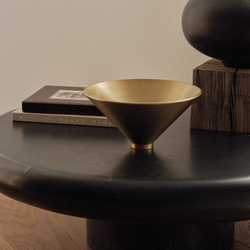 "Modern gold cone bowl on a sleek black table; elegant metallic finish enhances contemporary decor."