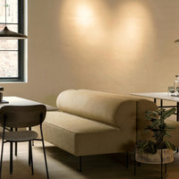Beige curved sofa with a smooth texture, surrounded by dark wood and greenery, enhancing a cozy, modern aesthetic.