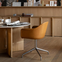 Tan leather office chair with a sleek silver base, set against warm wooden tones and a marble tabletop.