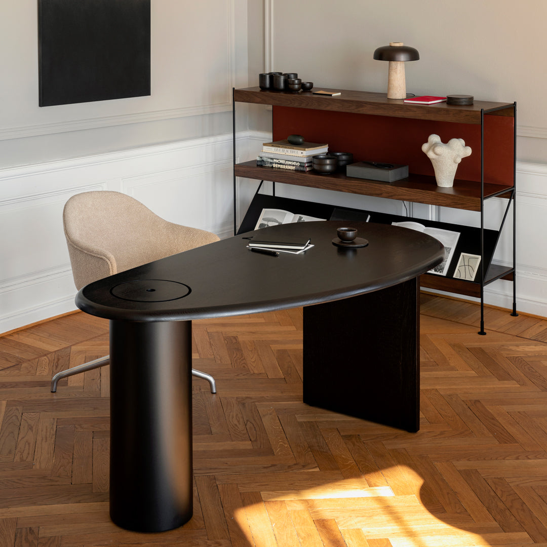 Modern black desk with a sleek oval shape, complemented by warm wood tones and a cozy beige chair.