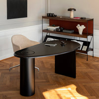 Modern black desk with a sleek oval shape, complemented by warm wood tones and a cozy beige chair.