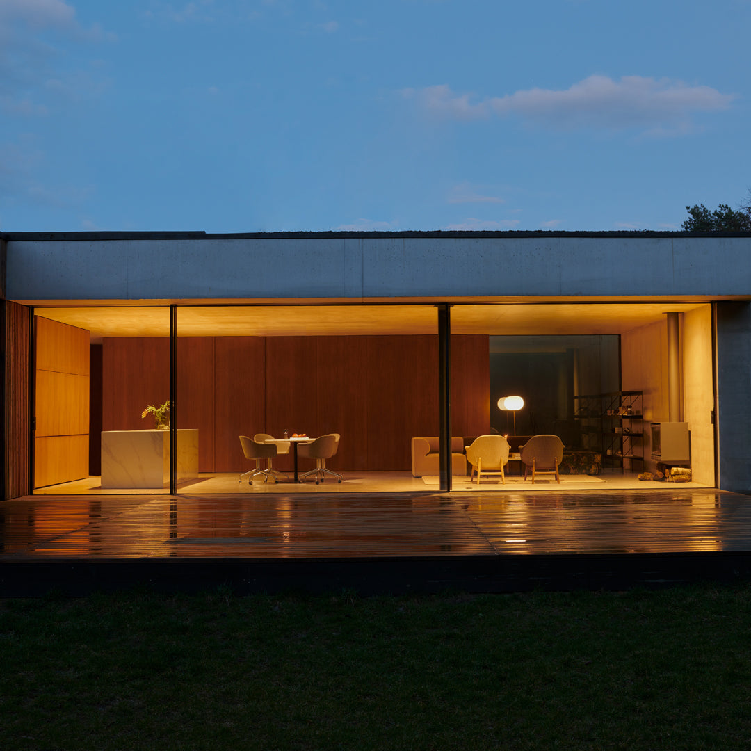 Modern home exterior with warm wood tones, sleek concrete, and illuminated glass accents against a twilight sky.
