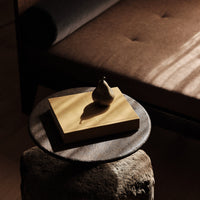 "Brown sofa, golden book, metallic pear sculpture on dark stone table, with soft shadows and warm lighting."